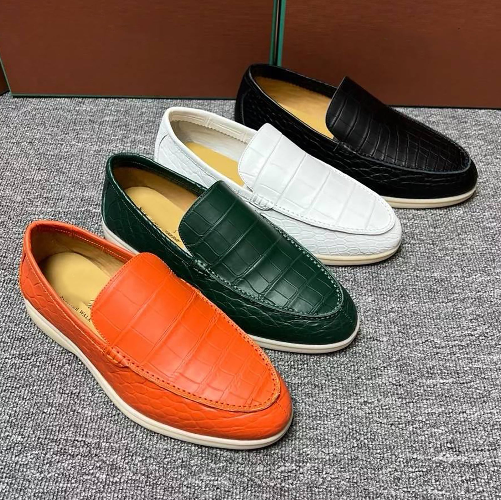 Four loafers in orange, green, white, and black on a textured surface.