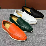 Four loafers in orange, green, white, and black on a textured surface.
