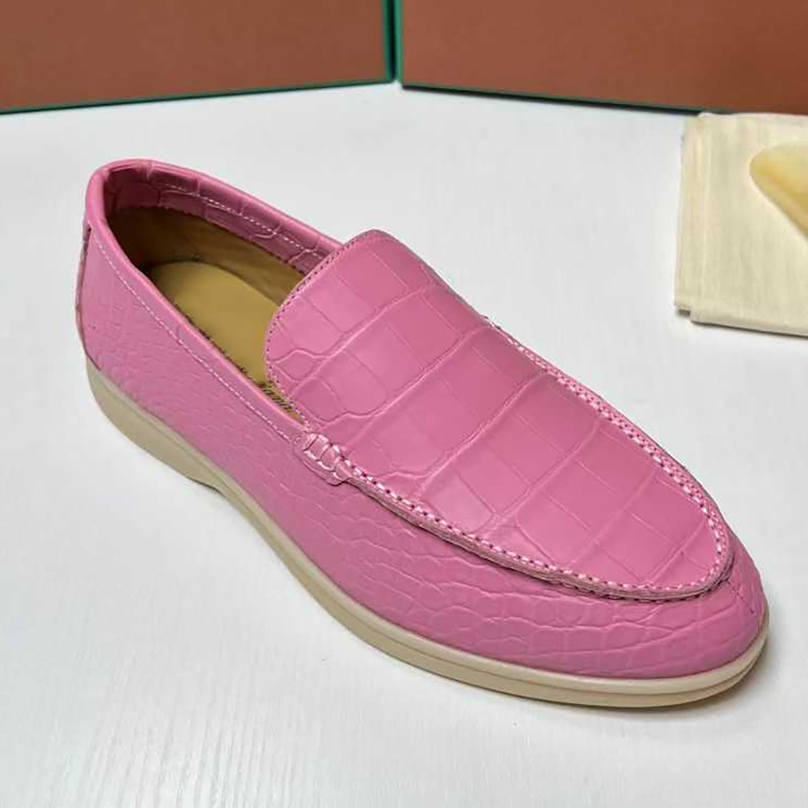 Pink loafer shoe on a white surface with a brown box in the background