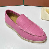 Pink loafer shoe on a white surface with a brown box in the background