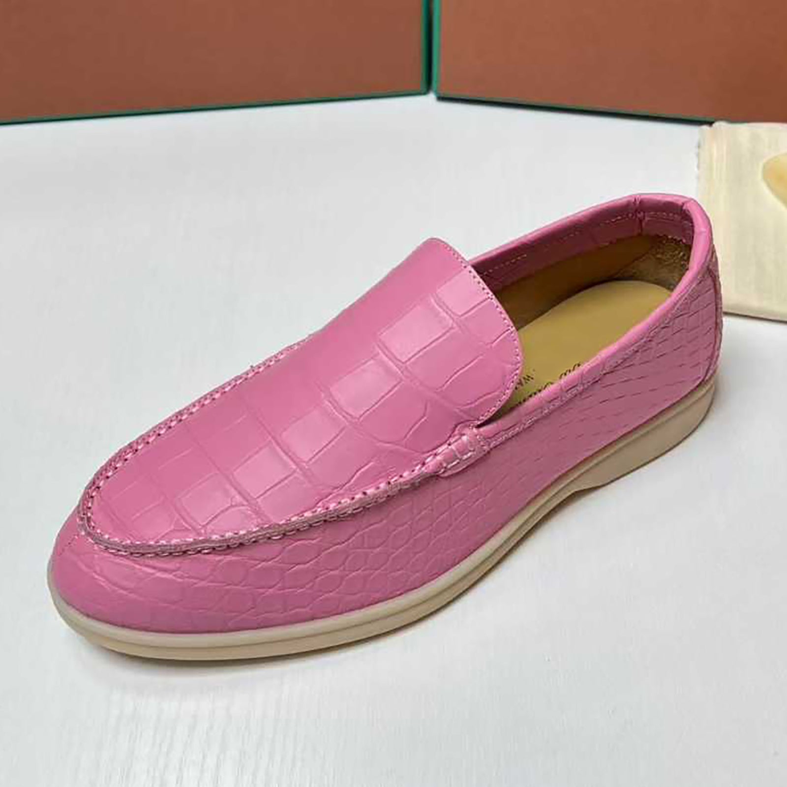 Pink loafer shoe on a white surface with a brown box in the background